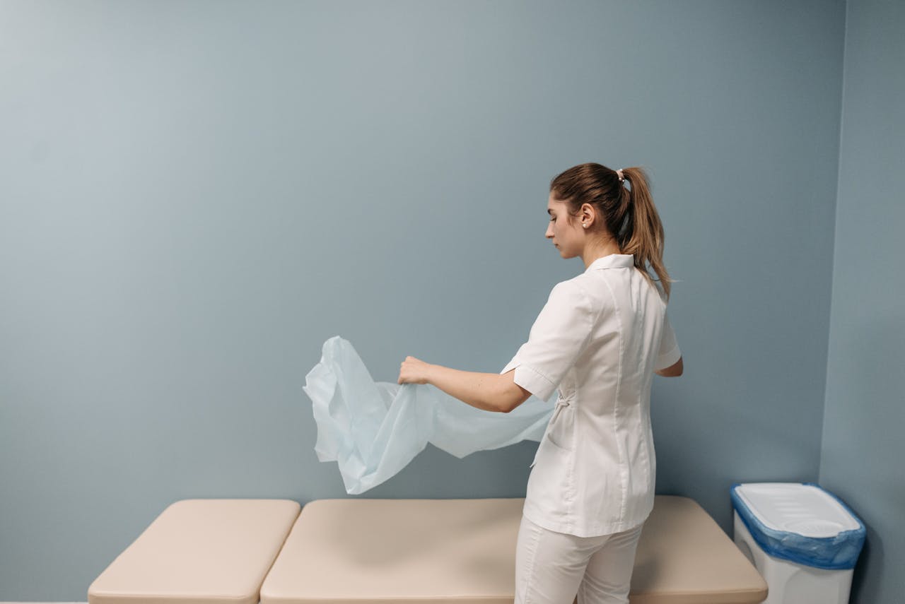 A nurse prepares an examination table in a healthcare facility, ensuring cleanliness and safety.